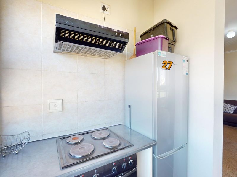 Compact kitchen area featuring a built-in electric hob, extractor fan, and tiled splashback, adjacent to an open-plan living space.