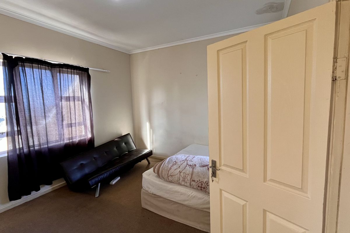 A standard bedroom featuring neutral wall tones, carpeted flooring, and a window with natural light exposure.