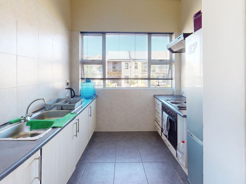 A functional galley-style kitchen featuring built-in cabinetry, tiled splashbacks, a stainless steel sink, and integrated cooking appliances with natural light from a large window.