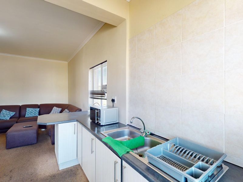 Open plan kitchen and living area featuring functional cabinetry, tiled backsplash, and a breakfast bar counter, seamlessly connecting to the adjacent lounge space.