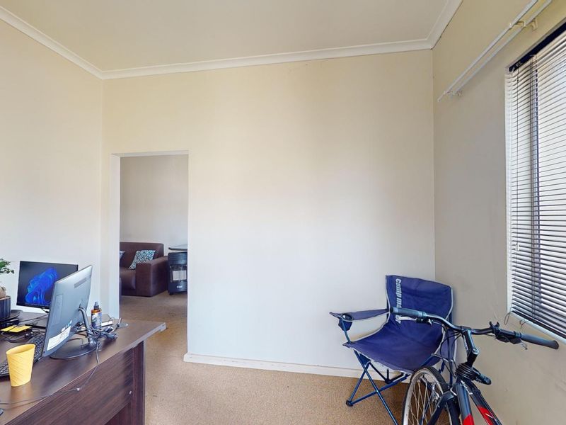 A functional office space featuring carpet flooring, neutral walls, and venetian blinds, offering a versatile area for work or study.