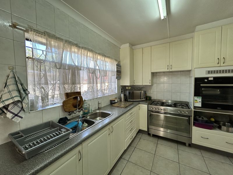 A functional kitchen featuring cream-colored cabinetry, a stainless steel gas hob, built-in oven, double basin sink, and tiled finishes throughout.
