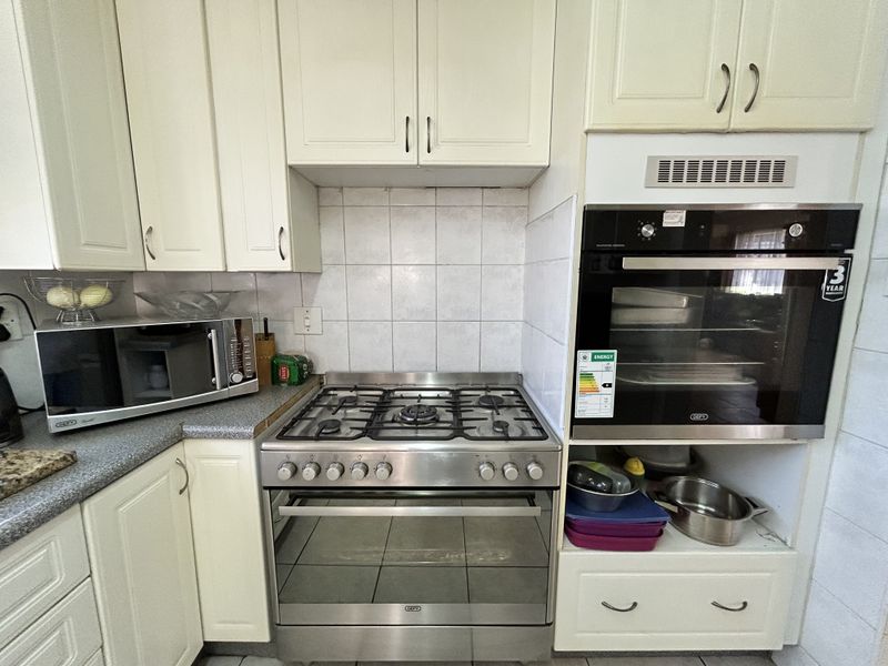 A functional kitchen area featuring cream-colored cabinetry, a stainless steel gas stove, and a built-in electric oven with tiled backsplash.