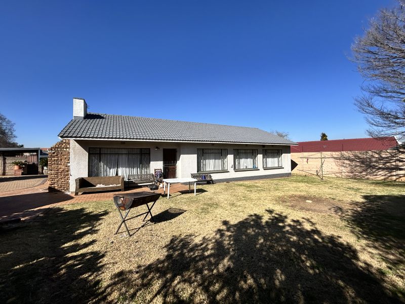 Rear view of the house featuring a tiled roof, brick chimney, and a paved patio area leading onto a spacious garden.