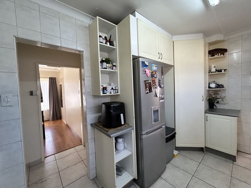 A functional kitchen area featuring built-in cabinetry, tiled walls, and tiled flooring, with an open doorway leading to an adjacent hallway.