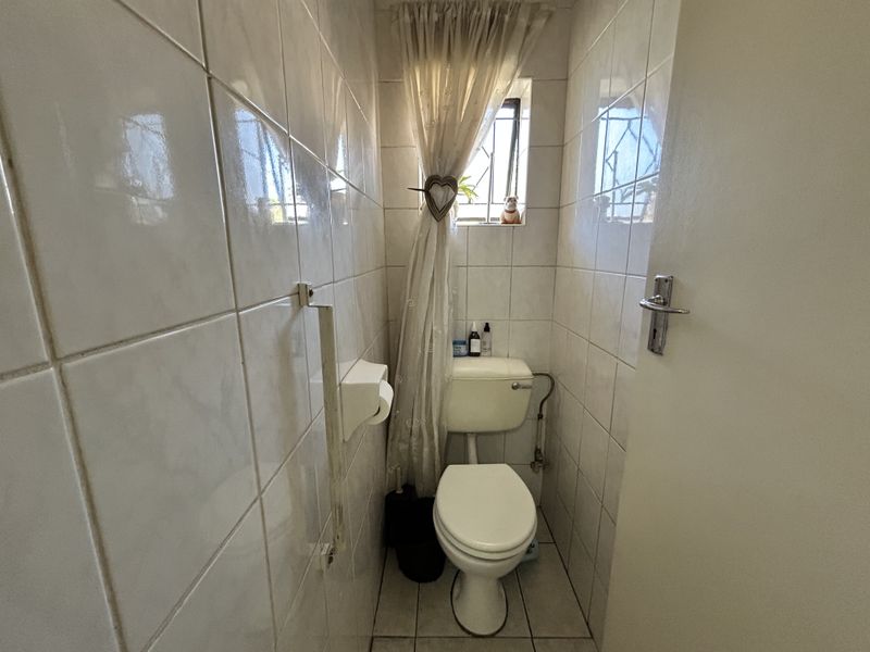 A compact guest bathroom featuring full-height ceramic wall tiling, a standard toilet, and a small window with security bars.