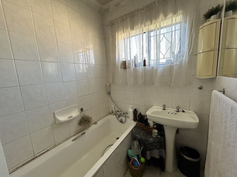 A functional bathroom featuring a standard bathtub, pedestal basin, and full-height wall tiling, offering potential for modernization and cosmetic updates.