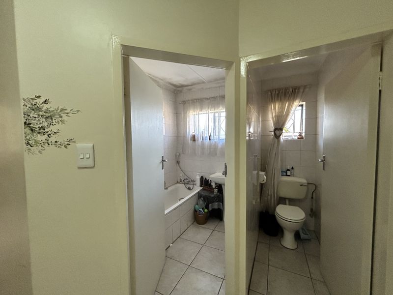 A functional bathroom layout featuring a separate toilet and a main bathroom area with a bathtub and pedestal basin, requiring cosmetic updates.