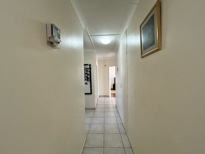 A clean and functional hallway featuring neutral tiled flooring and a wall-mounted prepaid electricity meter, providing access to various rooms in the home.