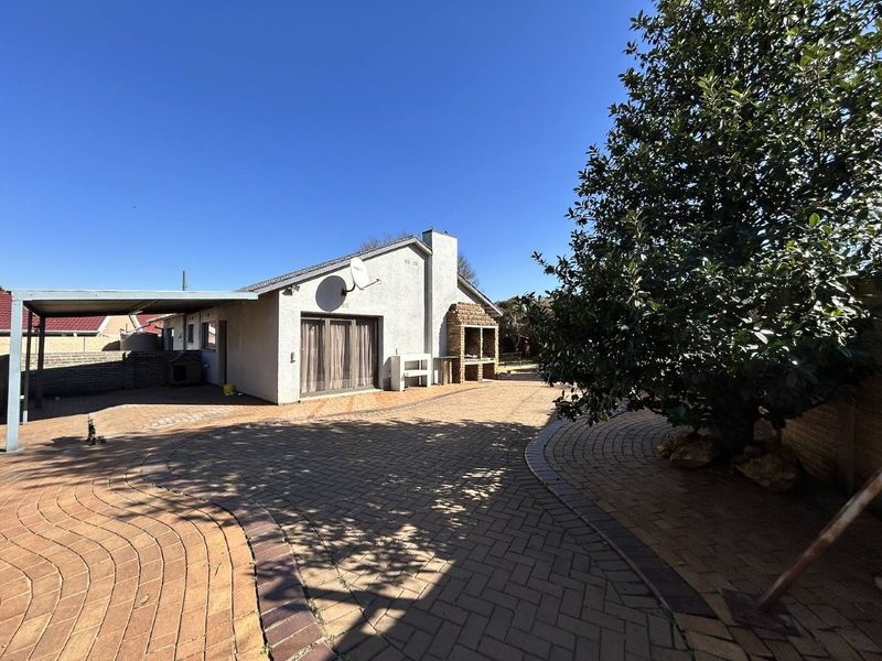 Rear exterior view featuring a paved courtyard, built-in braai area, and a covered carport structure.