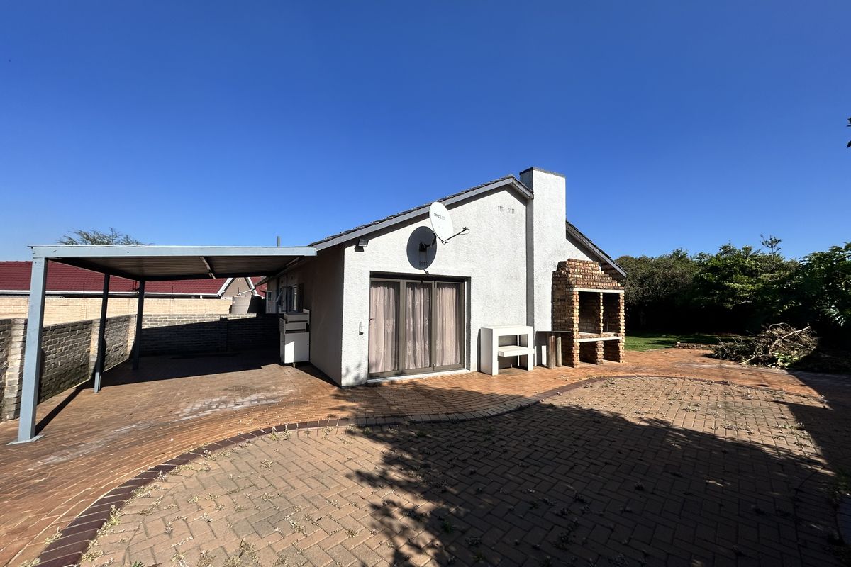 Rear exterior view featuring a brick-paved patio, a built-in brick braai, and a covered carport area with sliding door access to the home.
