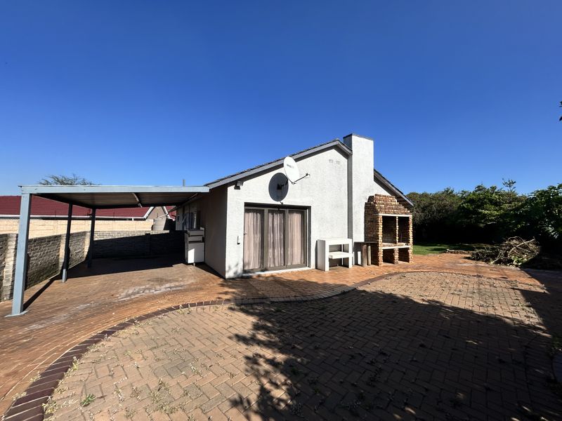 Rear exterior view featuring a brick-paved patio, a built-in brick braai, and a covered carport area with sliding door access to the home.