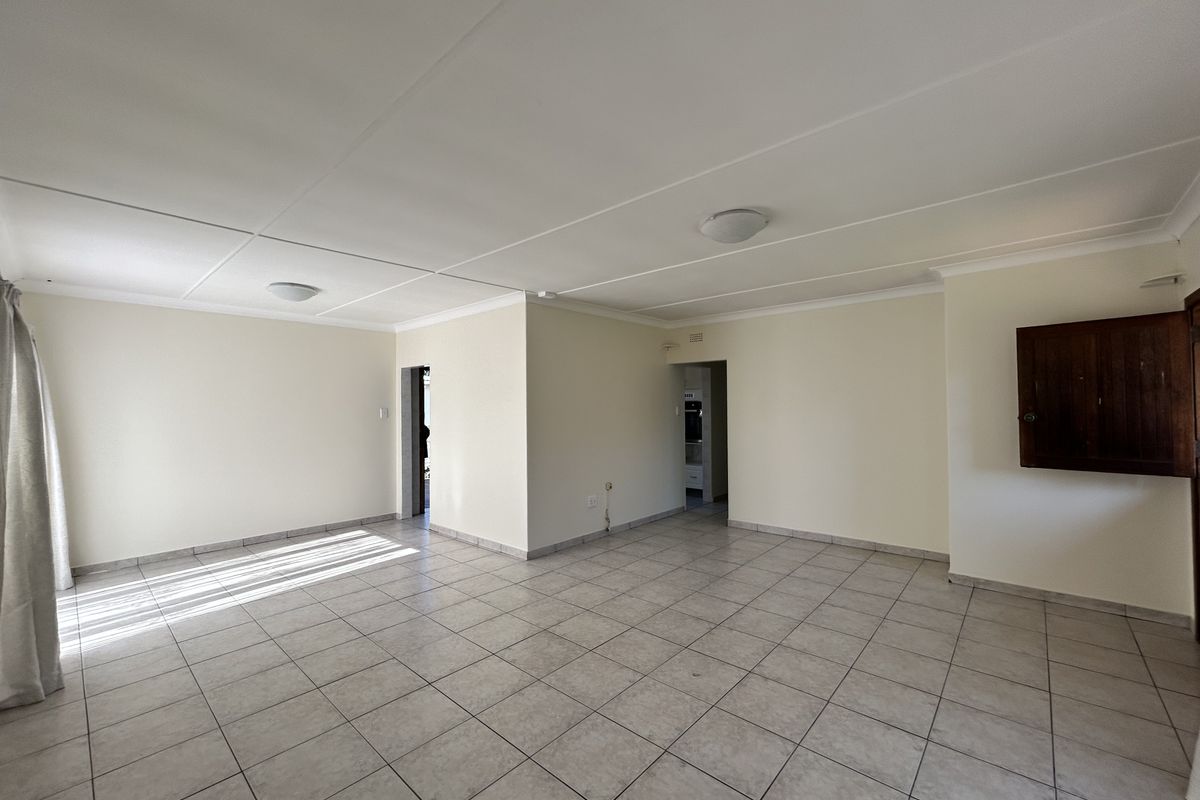 A spacious, empty living area featuring neutral tiled flooring, clean walls, and ceiling lighting, offering a versatile blank canvas for interior design.