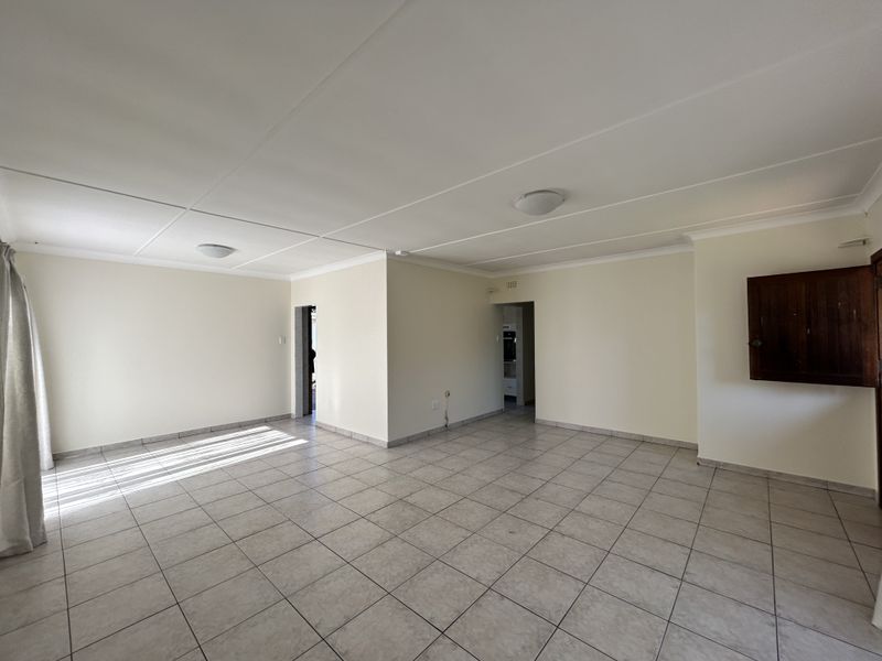 A spacious, empty living area featuring neutral tiled flooring, clean walls, and ceiling lighting, offering a versatile blank canvas for interior design.