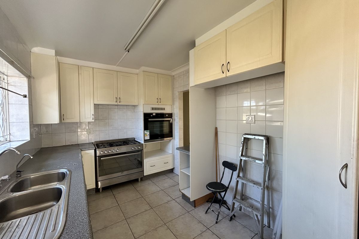 A functional kitchen featuring built-in cabinetry, a stainless steel double sink, gas stove, and built-in oven with tiled splashbacks and flooring.