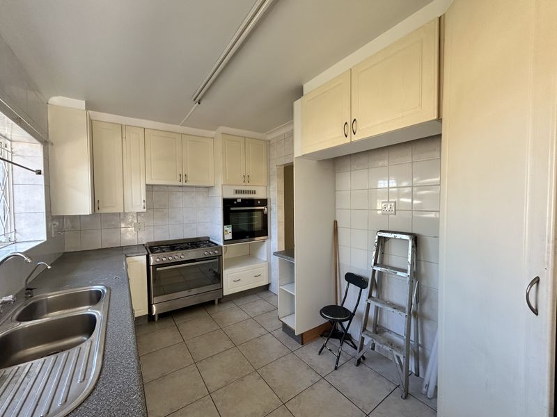 A functional kitchen featuring built-in cabinetry, a stainless steel double sink, gas stove, and built-in oven with tiled splashbacks and flooring.