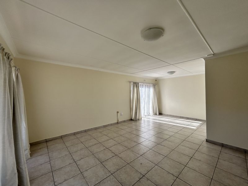 A spacious, empty living area featuring neutral tiled flooring, clean walls, and a sliding glass door providing natural light.