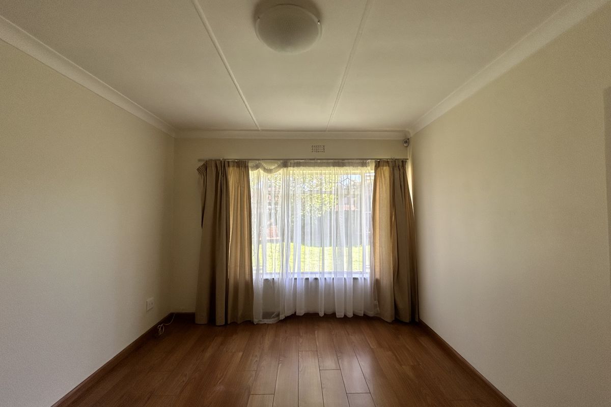 A bright, empty bedroom featuring laminate flooring, neutral walls, and a window with security bars, offering a clean canvas for personalization.
