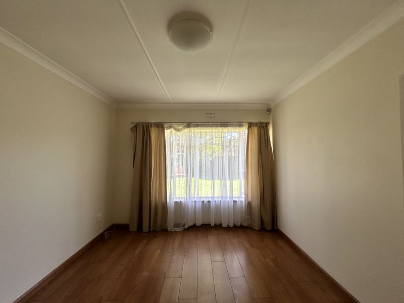 A bright, empty bedroom featuring laminate flooring, neutral walls, and a window with security bars, offering a clean canvas for personalization.