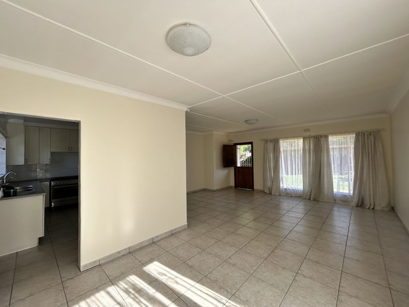 Spacious open-plan living area featuring tiled flooring, neutral walls, and direct access to an adjoining kitchen and outdoor space.