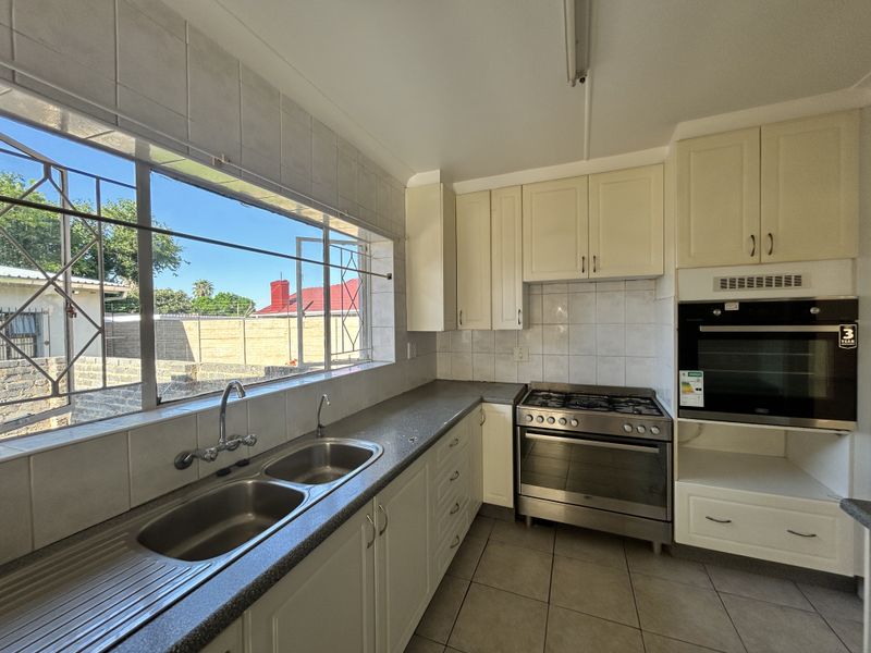 A functional kitchen featuring built-in cabinetry, a gas hob, a built-in oven, and a double bowl stainless steel sink with tiled splashbacks.
