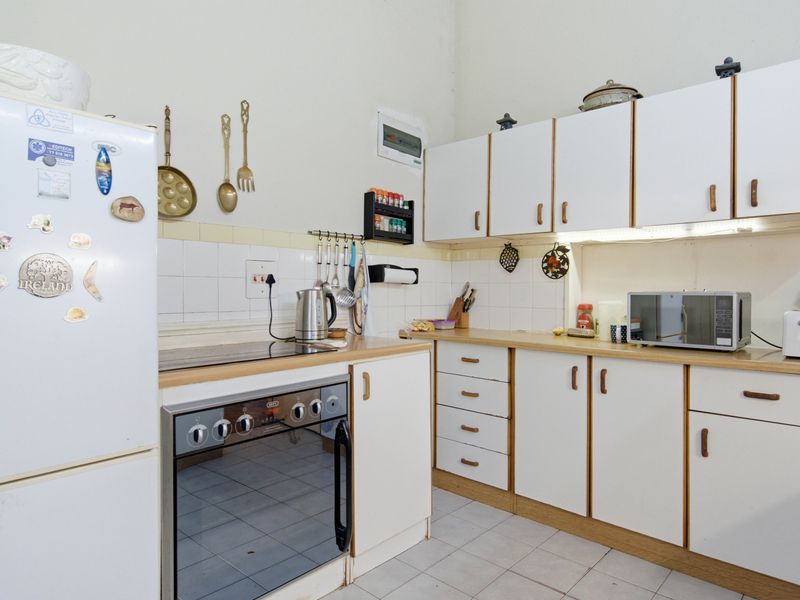 A functional kitchen featuring white cabinetry, laminate countertops, tiled backsplash, and built-in oven and hob, offering a practical layout with potential for modernization.
