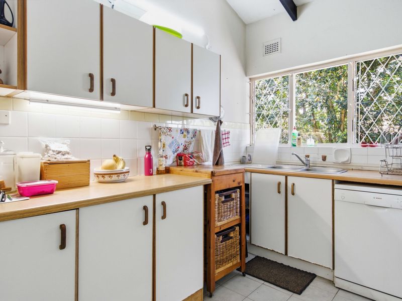 A functional kitchen featuring laminate countertops, tiled backsplash, double bowl sink, and ample built-in cabinetry with under-cabinet lighting.