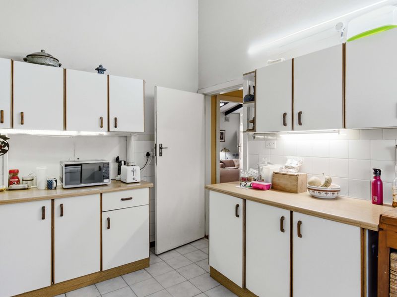 A functional kitchen featuring white cabinetry, laminate countertops, tiled backsplash, and tiled flooring with integrated under-cabinet lighting.