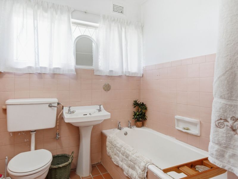A dated bathroom featuring pink wall tiles, a pedestal basin, a standard bathtub, and a toilet.