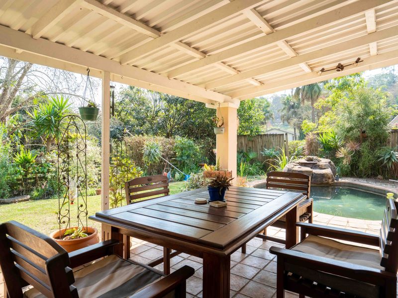 A covered outdoor patio area featuring tiled flooring, overlooking a private swimming pool and landscaped garden with a rock water feature.