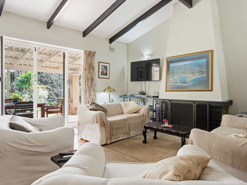 Spacious living room featuring exposed timber ceiling beams, a built-in fireplace, and large sliding glass doors providing seamless access to the outdoor patio area.