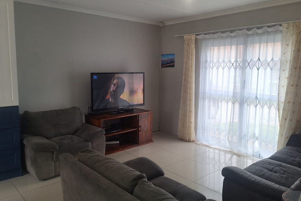 A comfortable living room featuring tiled flooring, built-in cabinetry, and a sliding glass door with a security gate leading to the exterior.