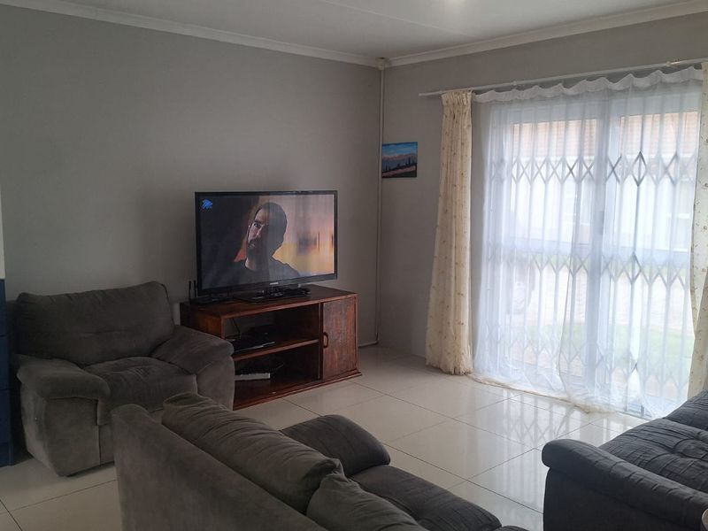 A comfortable living room featuring tiled flooring, built-in cabinetry, and a sliding glass door with a security gate leading to the exterior.