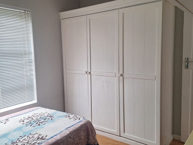 A well-maintained bedroom featuring a large built-in wardrobe, laminate flooring, and venetian blinds, offering a clean and functional living space.