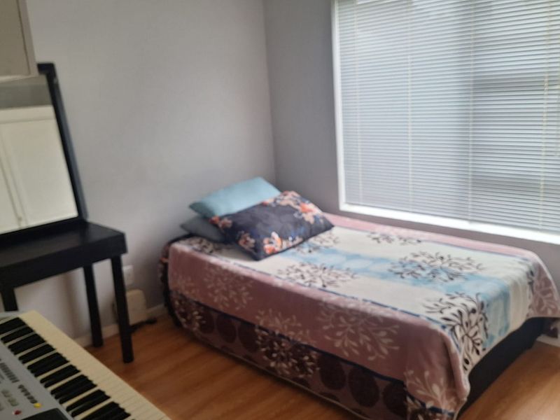 A compact bedroom featuring laminate flooring, a built-in cupboard, and a window fitted with venetian blinds.