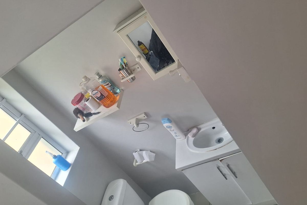 A compact bathroom featuring a vanity cabinet with basin, toilet, and wall-mounted storage. The space requires minor repairs to the vanity unit.