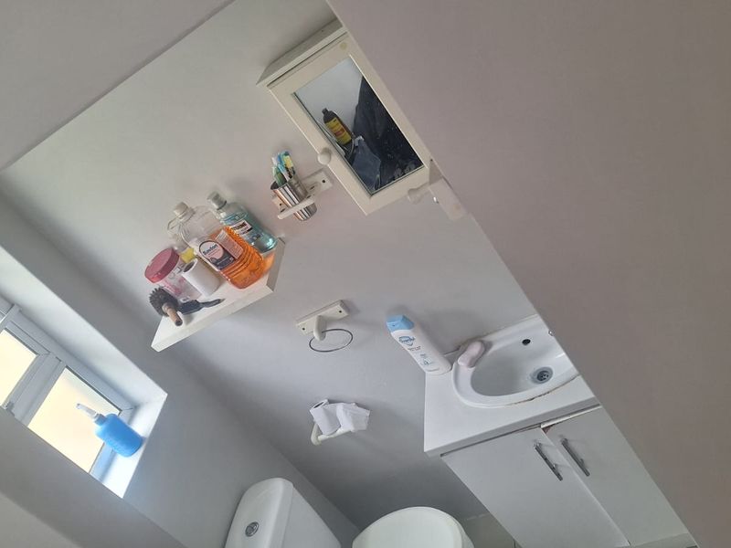 A compact bathroom featuring a vanity cabinet with basin, toilet, and wall-mounted storage. The space requires minor repairs to the vanity unit.