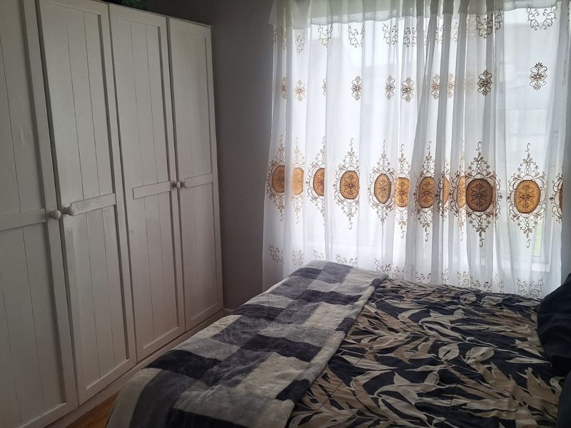 A bedroom featuring a white built-in wardrobe and natural light filtering through window curtains.