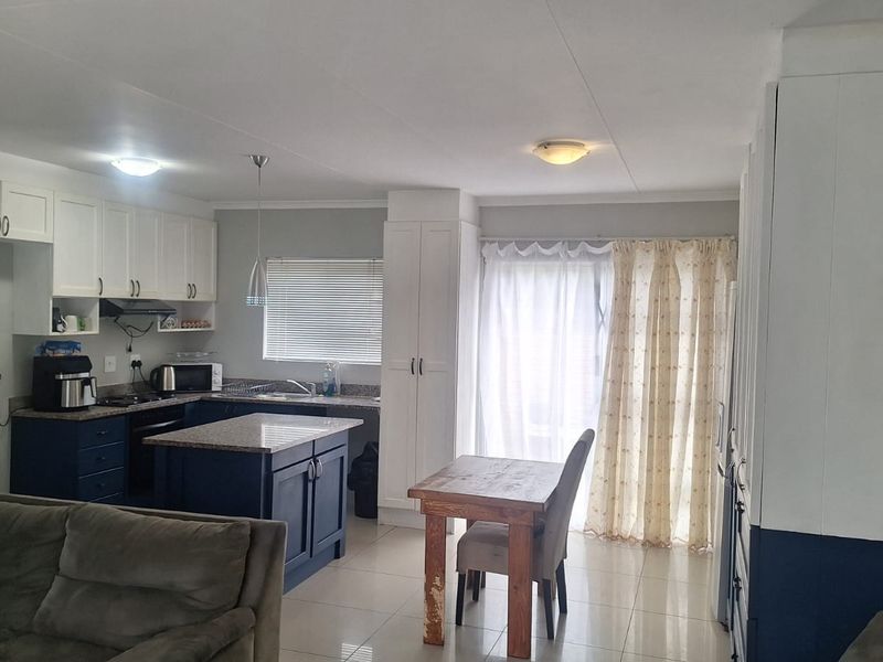 Open-plan living and kitchen area featuring modern two-tone cabinetry, granite countertops, a central island, and direct access to the patio through sliding glass doors.