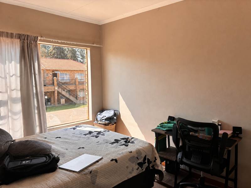 A sunlit bedroom featuring a large window with views of the apartment complex exterior.