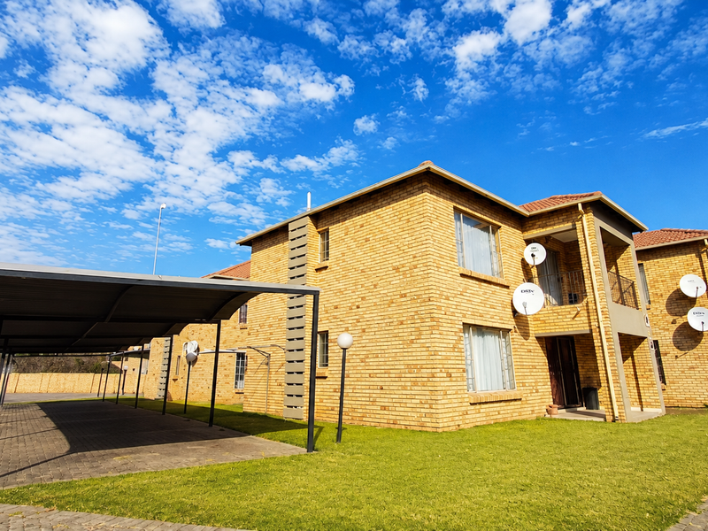 Exterior view of a multi-story face brick apartment complex featuring covered parking bays, paved driveways, and established lawn areas.