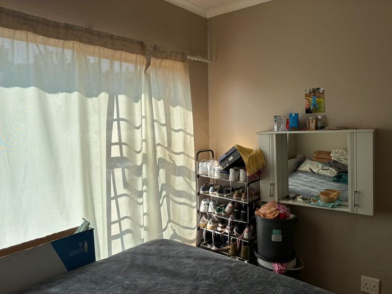 A bedroom featuring a window with a curtain rail and a wall-mounted mirror cabinet, providing functional storage and natural light.