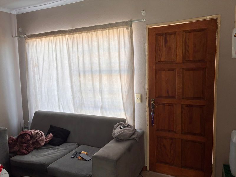 A living room area featuring a solid timber panel door and a window with a curtain rod, showing signs of wear on the wall surfaces.