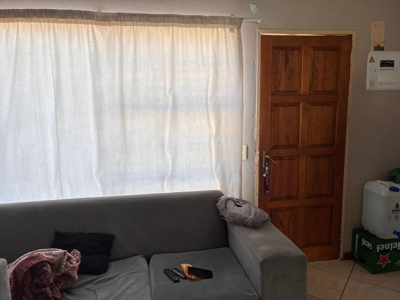 A living room area featuring tiled flooring and a timber panel door, showing signs of wear and minor structural damage near the electrical board.
