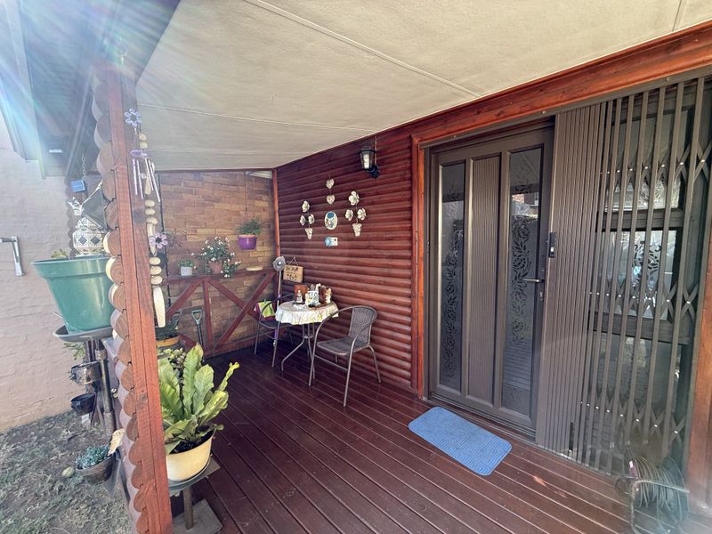 A covered patio area featuring timber decking, log-style wall cladding, a brick feature wall, and a secure sliding glass door entrance.