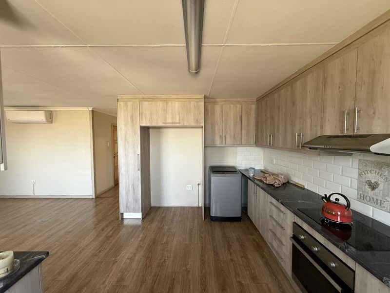 Open-plan kitchen and living area featuring modern wood-look cabinetry, subway tile backsplash, integrated appliances, and laminate flooring throughout.