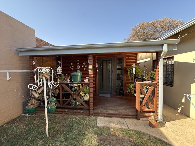 A covered timber deck patio featuring log-style wall cladding, a secure entrance door, and integrated timber balustrades, providing a functional outdoor living space.