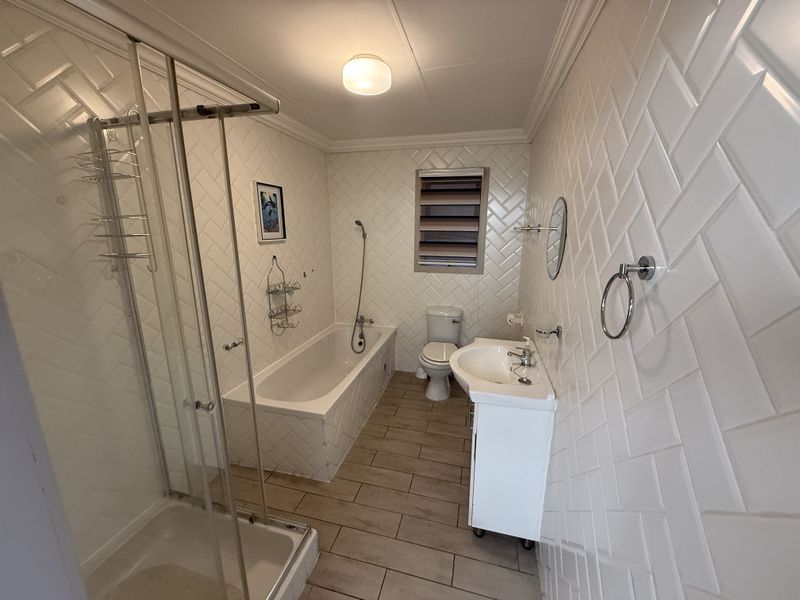 Modern bathroom featuring a glass shower enclosure, built-in bathtub, pedestal washbasin, and stylish herringbone wall tiling.