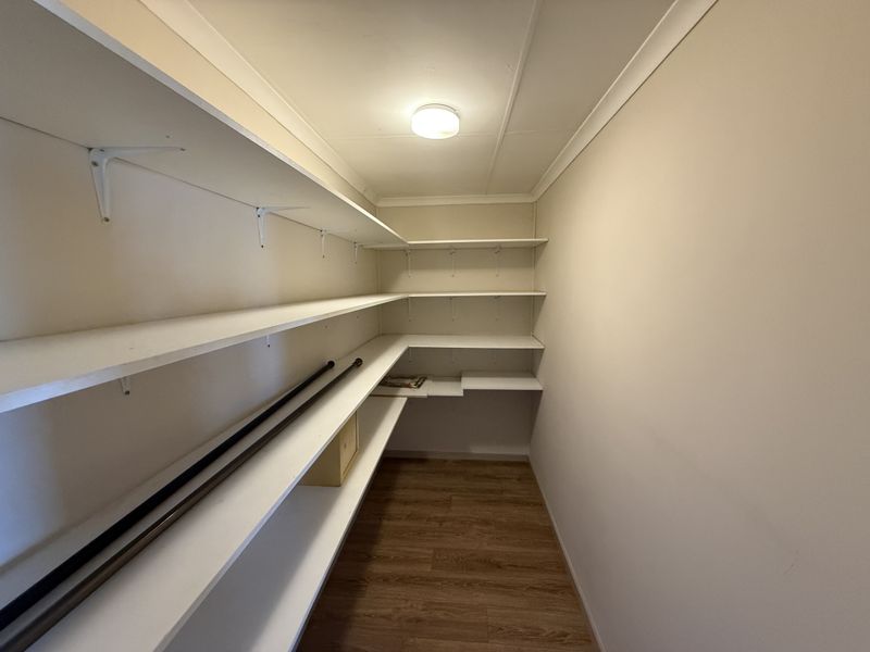 A clean and functional walk-in storage or pantry area featuring extensive built-in shelving and durable laminate flooring.