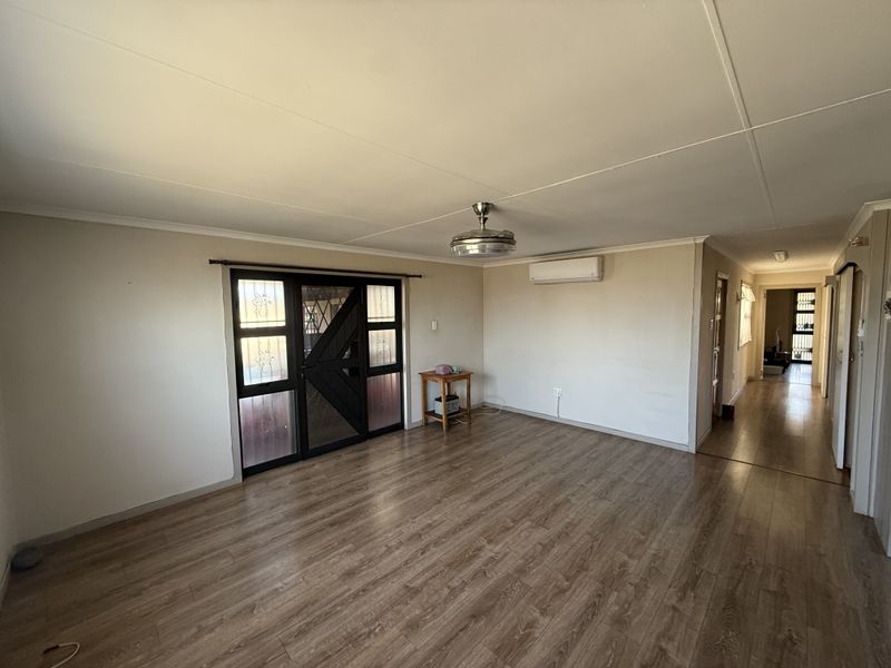 Spacious living area featuring laminate flooring, a ceiling fan, and a wall-mounted air conditioning unit, leading to a hallway and exterior access.